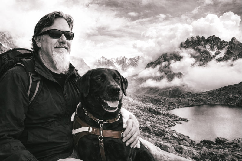 Ted, a middle aged man with a long white goatee and his guide dog a black lab Fauna in the maintains. 